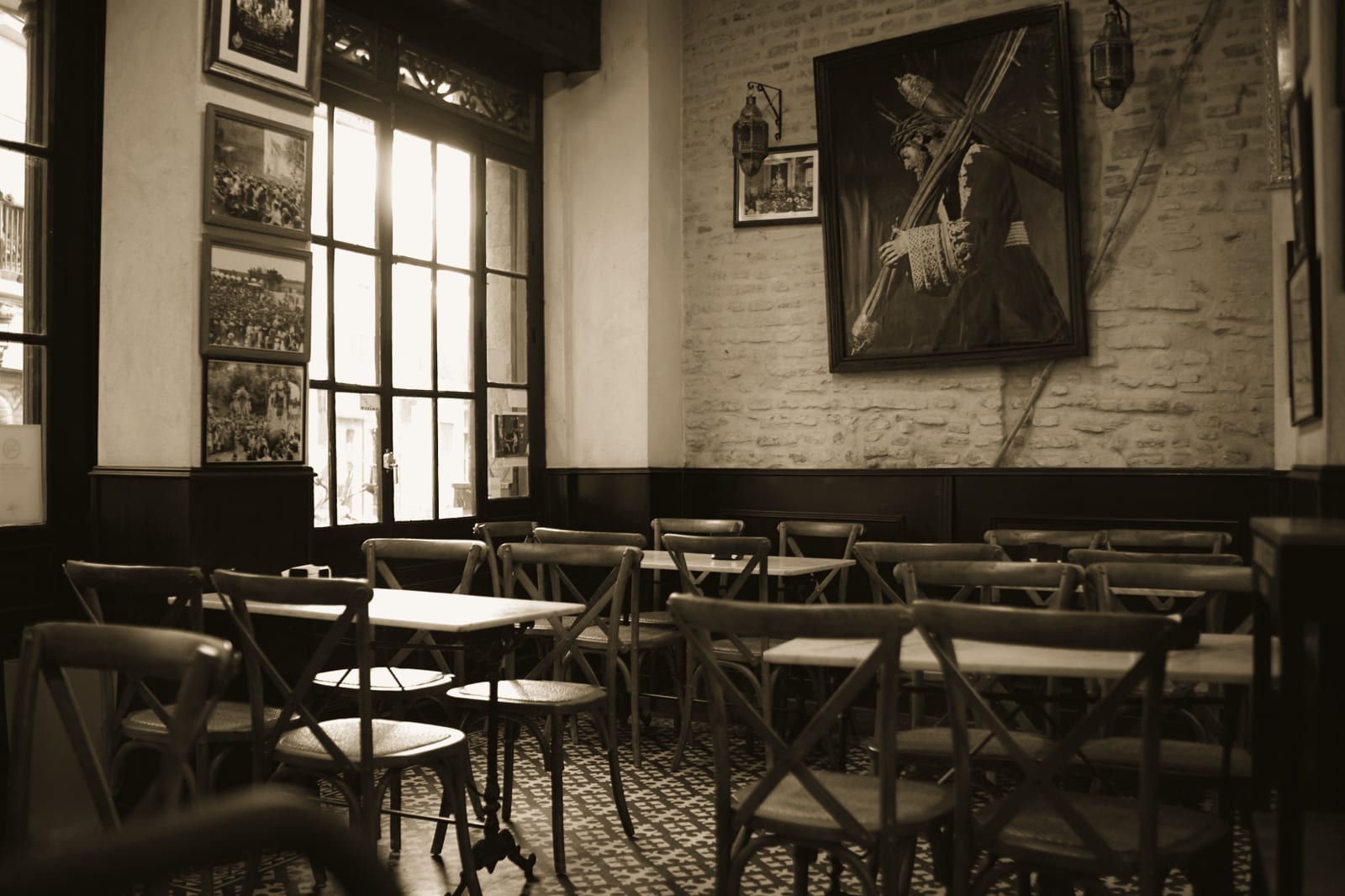 Sala di un caffè con sedie di legno curvato, tavolini tondi e una grande vetrata a sinistra.